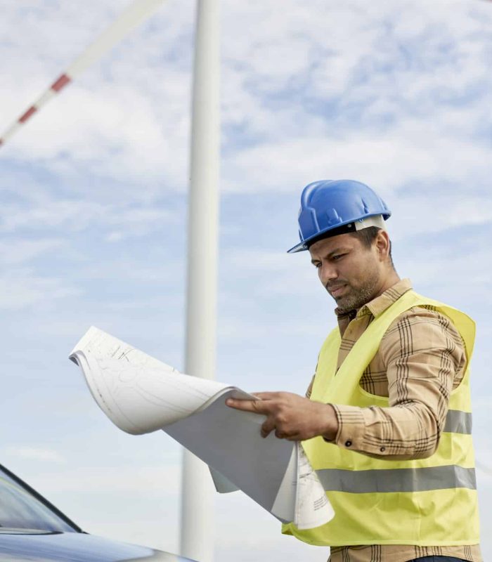 Latin male engineer standing on wind turbine field and checking paper project