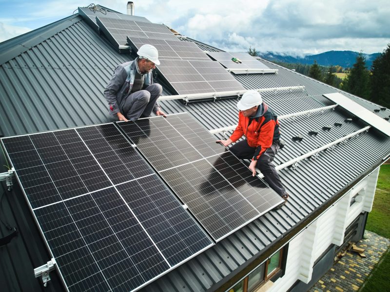 Men workers installing solar panels on roof of house.