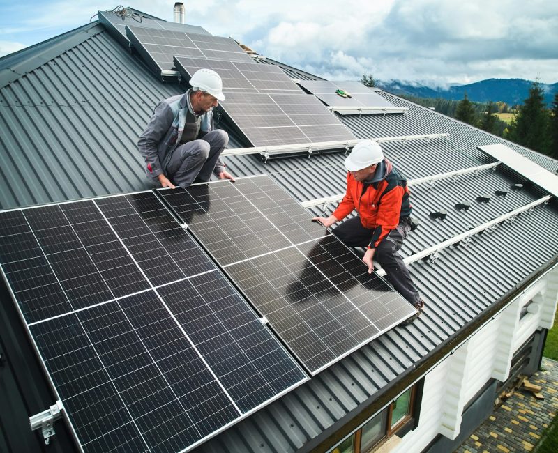 Men workers installing solar panels on roof of house.